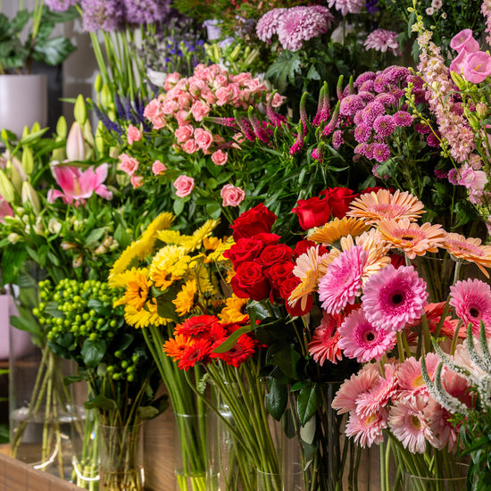 Display of colorful flower bouquets in clear vases on a wooden shelf