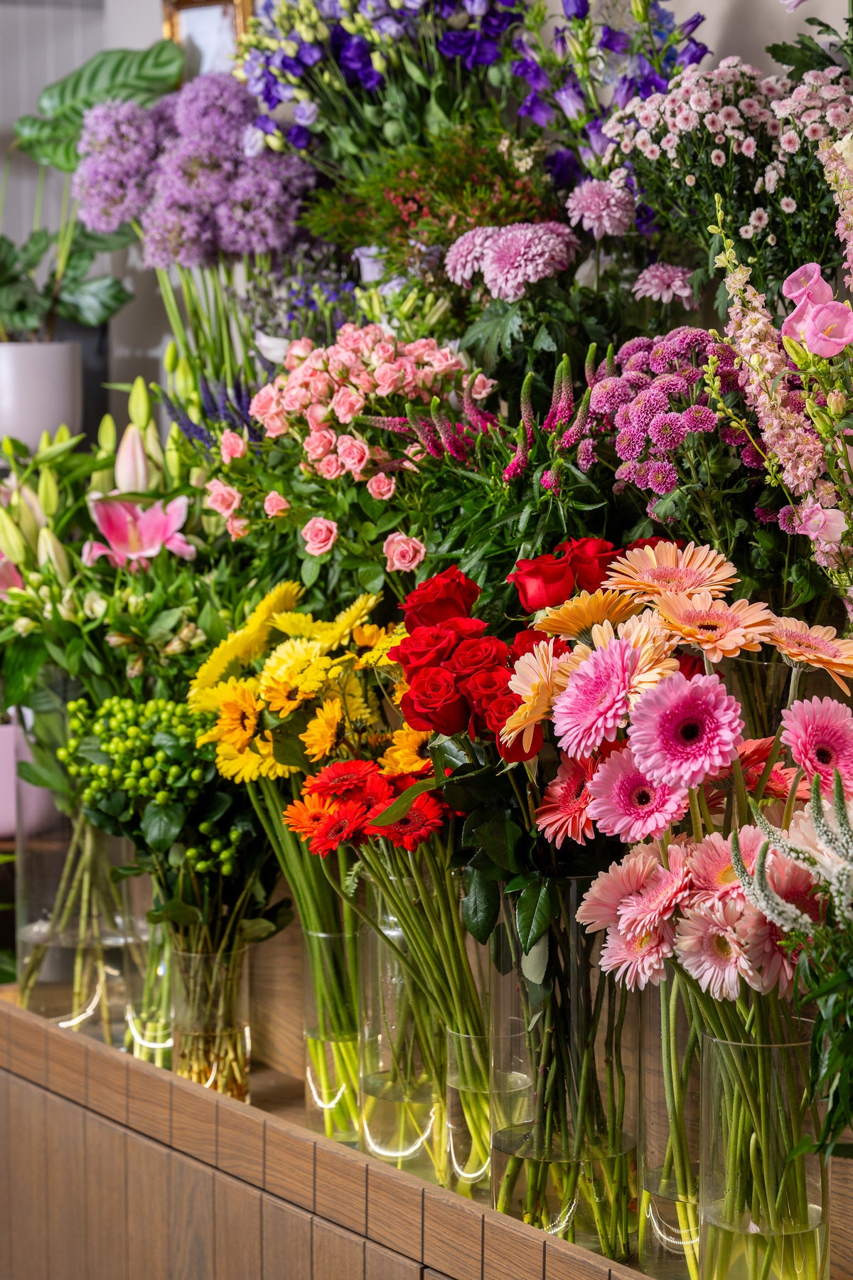 Display of colorful flower bouquets in clear vases on a wooden shelf
