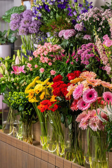 Display of colorful flower bouquets in clear vases on a wooden shelf