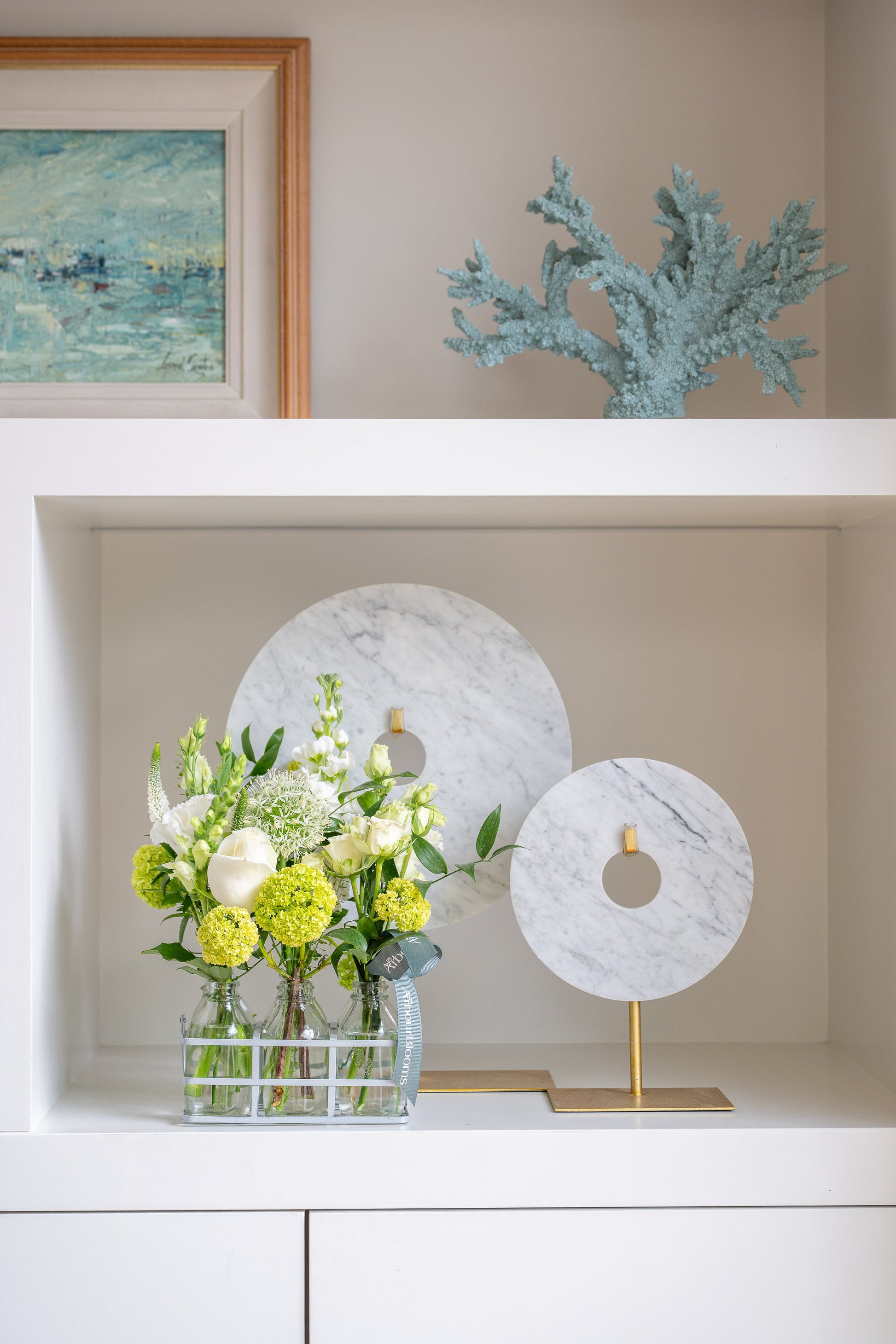 Decorative shelf with a floral arrangement, marble ornaments, and a framed painting