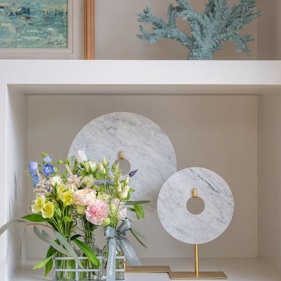 Decorative shelf with a floral arrangement, marble sculptures, and a framed painting