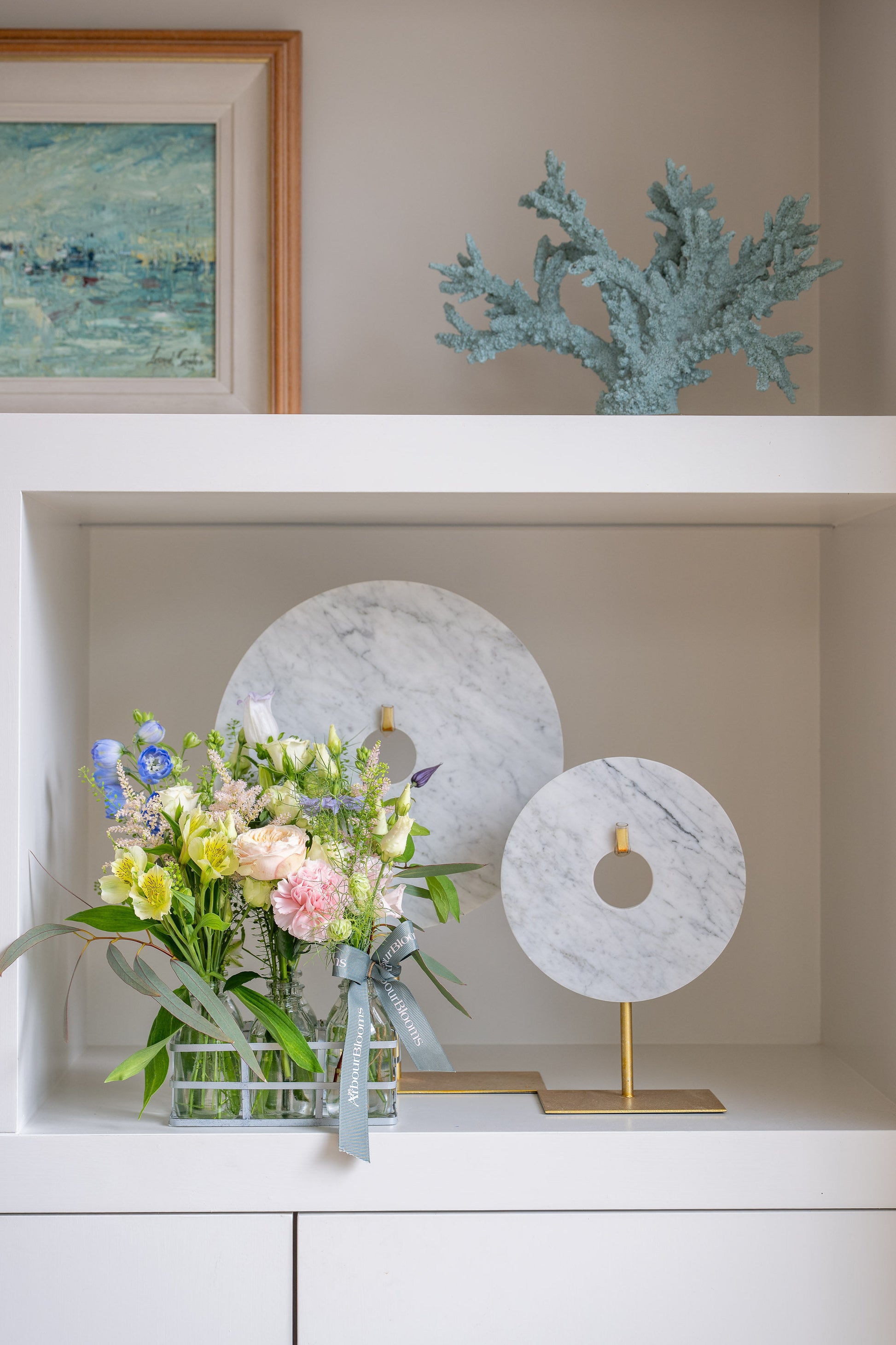 Decorative shelf with a floral arrangement, marble sculptures, and a framed painting