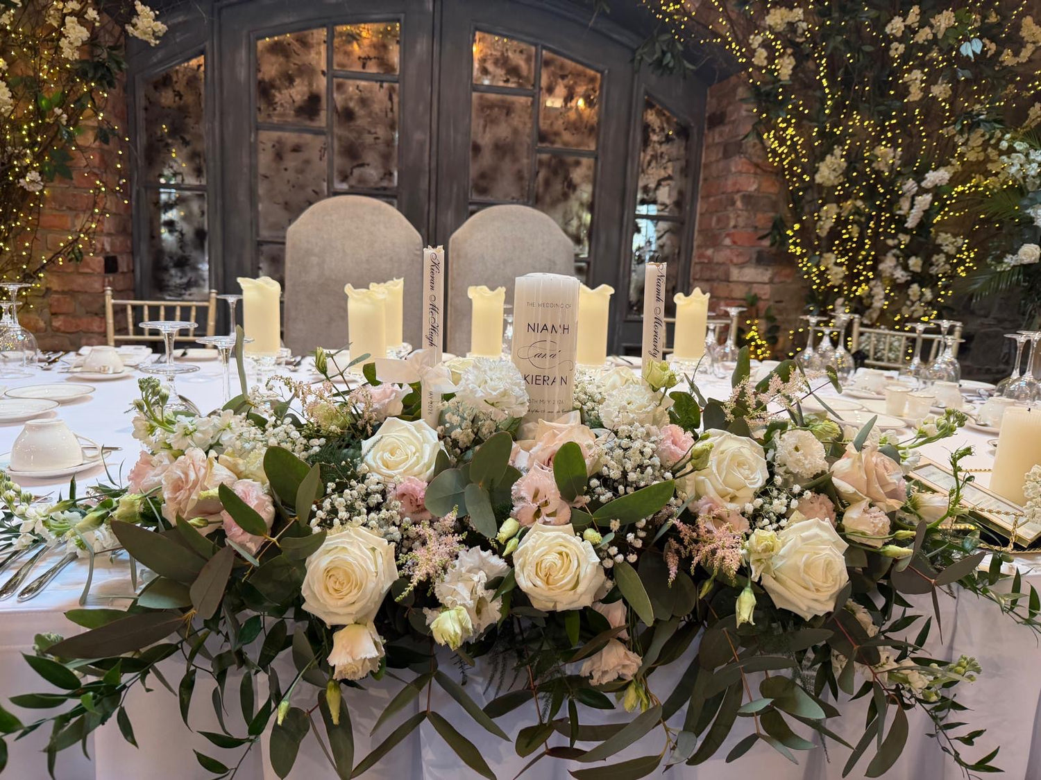 Wedding table setting with floral arrangements and candles in a room with large windows